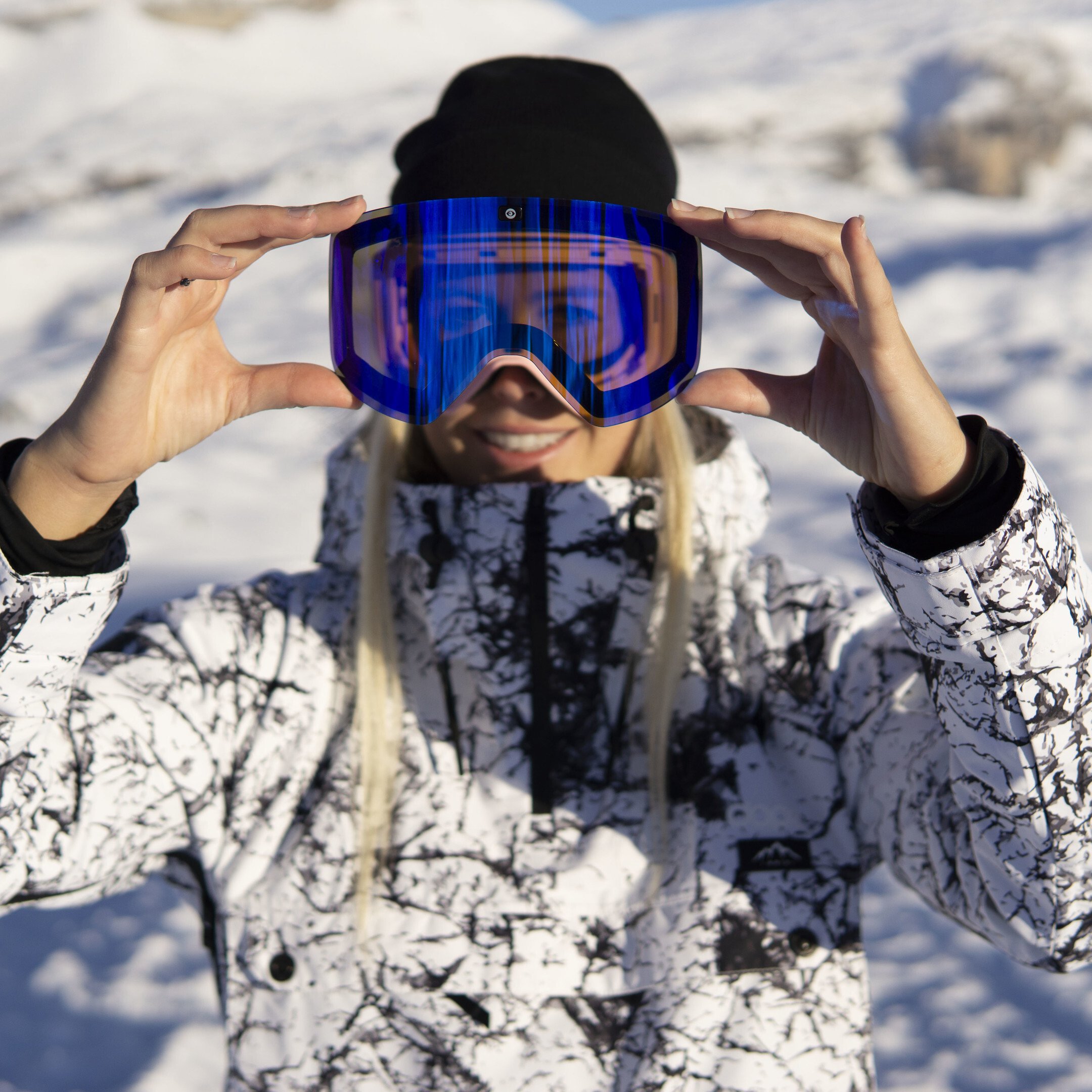 In action: Athlete demonstrating the interchangeable lens of ski goggles JAMIE Baby Pink, blue lens, pink design strap visible.